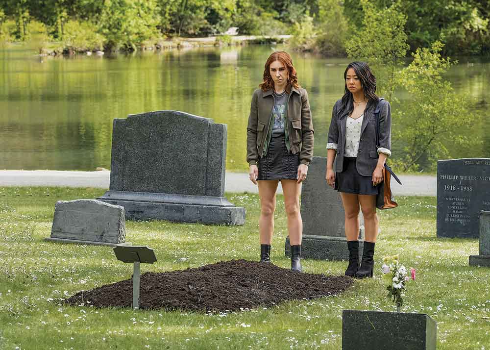 Laid on W Network. Pictured: AJ (Zosia Mamet) and Ruby (Stephanie Hsu) stand graveside.