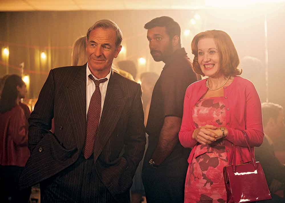 Grantchester on Masterpiece on PBS. Pictured: Alphy (Rishi Nair) with lovably gruff police detective Geordie Keating (Robson Green) and his wife Cathy (Kacey Ainsworth).