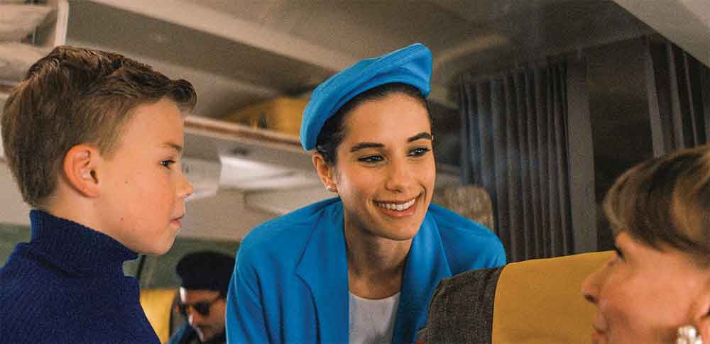 Propeller One-Way Night Coach on Apple TV. Pictured: Young airplane enthusiast Jeff (Clark Shotwell) chats with flight attendant Doris (Ella Bleu Travolta).